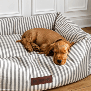 Cocker spaniel descansando sobre cama desenfundable para perros con diseño de rayas gris y beige acolchada y confortable.