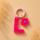 Chapa identificativa para perros con inicial L personalizada y nombre Lola en color rosa flúor con colgante flor decorativo.