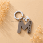 Chapa identificativa personalizada para perros con inicial letra M en color gris, nombre troquelado Meliton, colgante decorativo de caniche y anilla blanca.