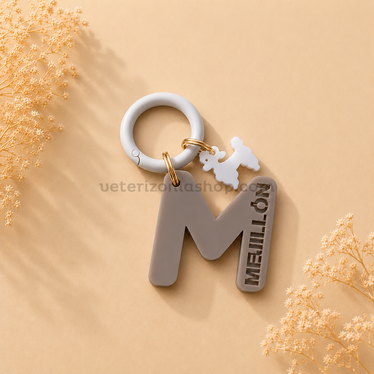 Chapa identificativa personalizada para perros con inicial letra M en color gris, nombre troquelado Meliton, colgante decorativo de caniche y anilla blanca.