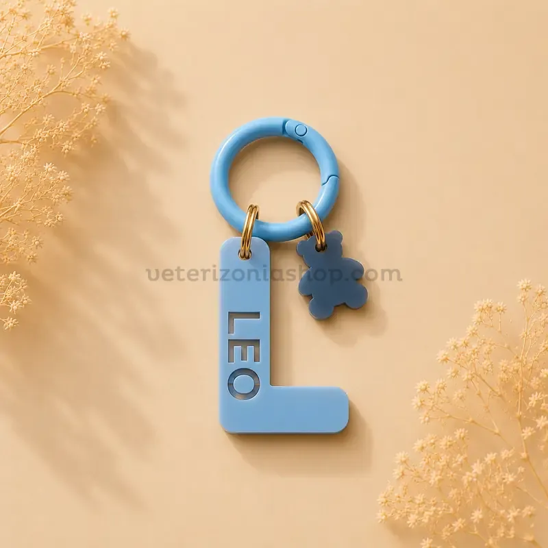 Chapa identificativa personalizada para perros con inicial L azul cielo, nombre Leo troquelado y colgante decorativo de osito sobre fondo beige.