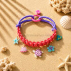 Collar con charms para perros pequeños modelo Océano Coral en tonos coral y lila con colgantes marinos decorativos sobre fondo arena estilo verano
